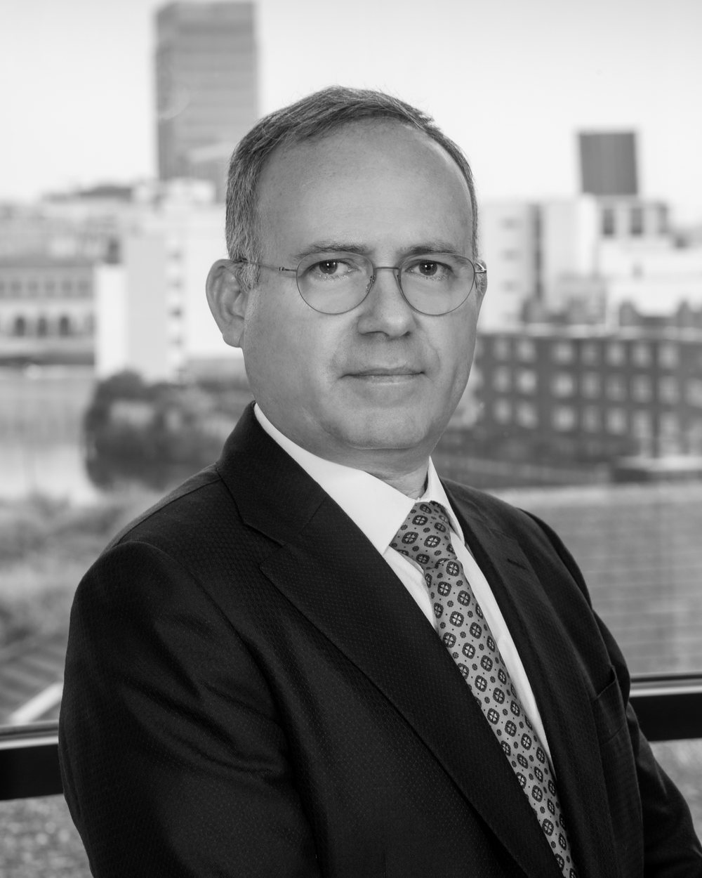 Portrait of Giuseppe Pancucci in a dark suit, in front of an office window overlooking the city.